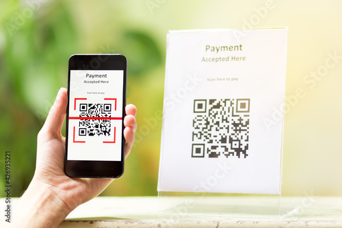 Close up of a hand holding smartphone and scanning the qr code to make a payment. Cashless technology concept