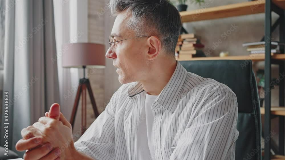 Close up portrait of pensive middle aged man in eyeglasses sitting at wokplace and rubbing hands, slow motion Close up portrait of pensive middle aged man in eyeglasses sitting at wokplace and rubbing hands, slow motion