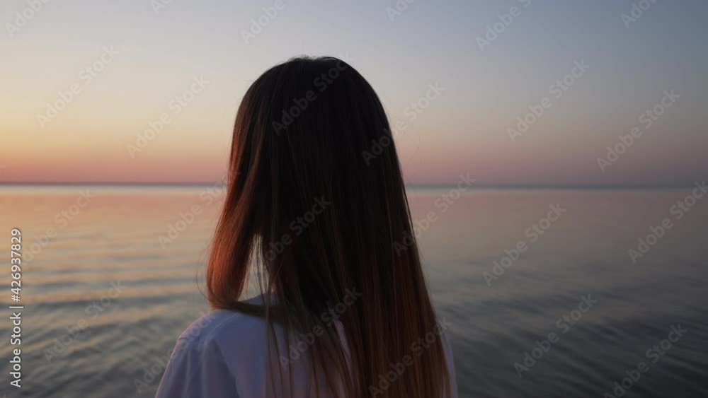 Beautiful woman of European ethnicity at sunset. Coastline of the sea on which stands a happy girl and smiles at the camera. Slow motion 4K video of a romantic landscape. Beautiful woman of European ethnicity at sunset. Coastline of the sea on which stands a happy girl and smiles at the camera. Slow motion 4K video of a romantic landscape.