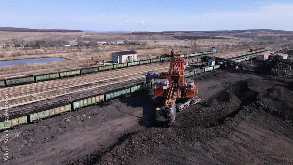 2021, Novoshakhtinsky, Russia - Extraction of coal. View from above. A large rotary excavator shovels coal from a coal heap with a bucket. Loading coal into railway wagons. 2021, Novoshakhtinsky, Russia - Extraction of coal. View from above. A large rotary excavator shovels coal from a coal heap with a bucket. Loading coal into railway wagons.