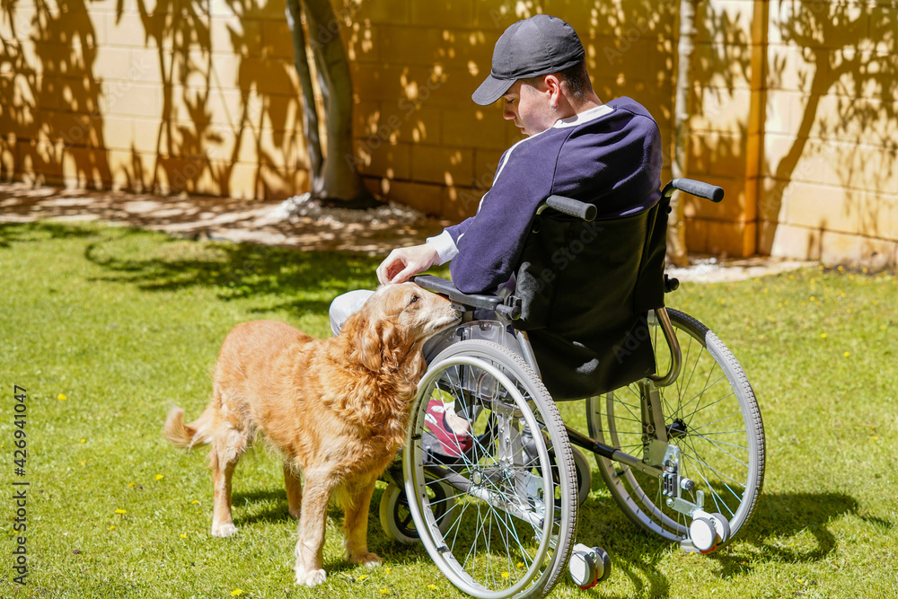 Disabled young man sitting in a wheelchair and taking fresh air in his garden and enjoying life. Disabled young man sitting in a wheelchair and taking fresh air in his garden and enjoying life.