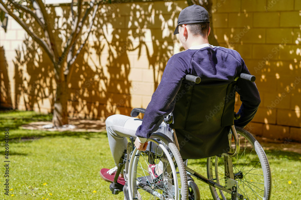 Disabled young man sitting in a wheelchair and taking fresh air in his garden and enjoying life.
