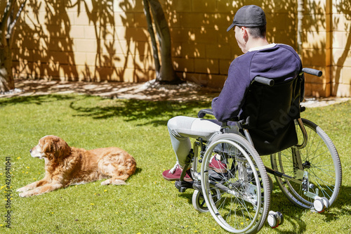 Disabled young man sitting in a wheelchair and taking fresh air in his garden and enjoying life. © JuanFrancisco