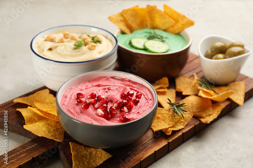 Different kinds of tasty hummus served with nachos on light table
