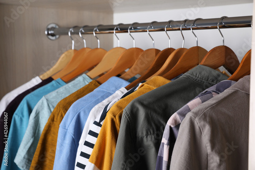 Different stylish clothes hanging on rack in wardrobe