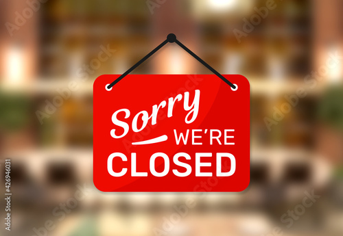 Hanging sign for shop with text Sorry we're closed on blurred restaurant background.