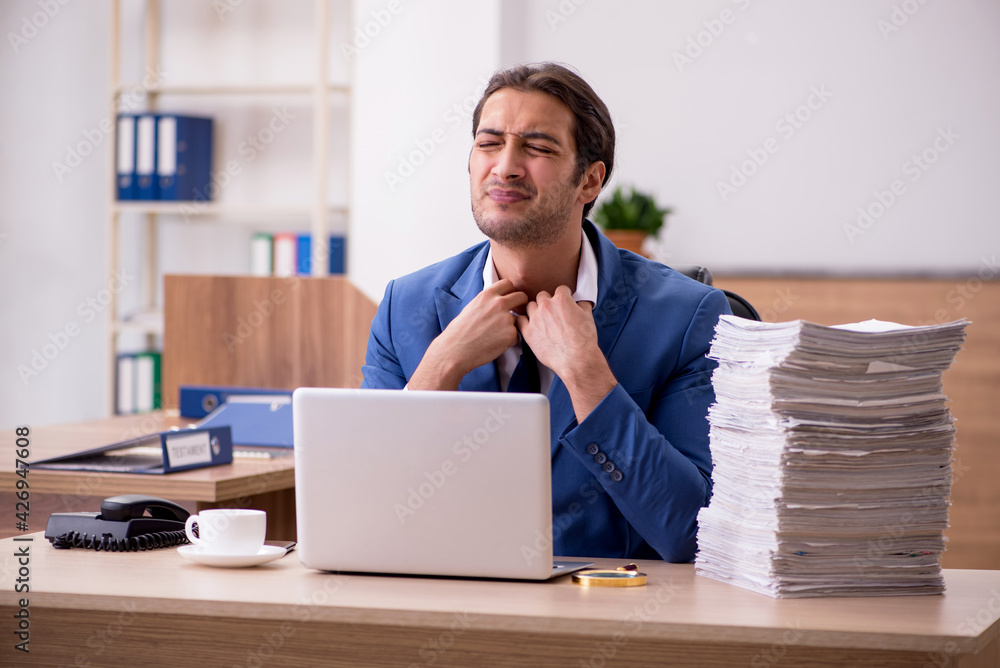 Young male employee unhappy with excessive work in the office Young male employee unhappy with excessive work in the office
