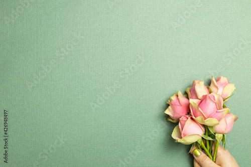 Fototapeta Naklejka Na Ścianę i Meble -  Hand holding pink rose flowers on green background. flat lay, top view, copy space