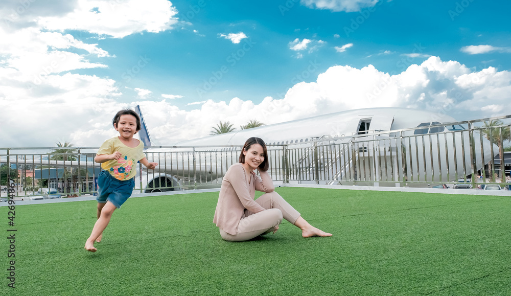 Fototapeta premium Asian woman mother smiling looking at the camera With little child running around with a plane and blue sky background, happy family relaxes time concept