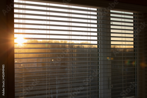 Vue des stores d'une fenêtre en gros plan avec coucher de soleil flou en arrière plan