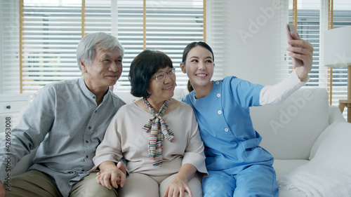 Young senior asia citizen couple and assisted home living nurse care hold mobile phone selfie videocall online at home apartment on sofa couch in virtual digital telehealth telemedicine concept. photo