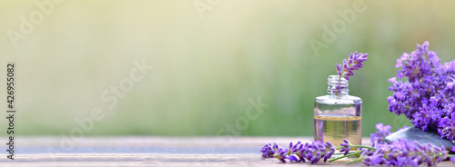 bottle of essential oil and lavender flowers arranged on a wooden table on blur background