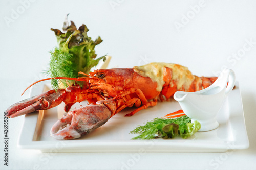 Cooked lobster with grilled cheese, lettuce leaves, dill or fennel, lemon and oily sauce in gravy boat. Fancy cuisine food. Side view