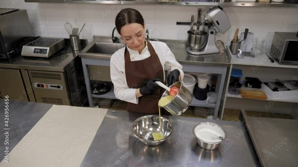 A female chef prepares a mousse cake, pours pistachio mousse into a bowl. A female chef prepares a mousse cake, pours pistachio mousse into a bowl.