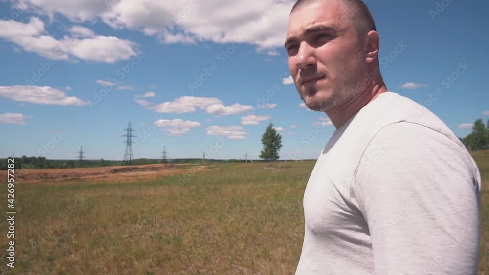 A serious bald man who looks like an athlete appears in the frame, looks around and leaves. In the background Sky, clouds, trees, power lines. The concept of a lost person, prison escaped, escape A serious bald man who looks like an athlete appears in the frame, looks around and leaves. In the background Sky, clouds, trees, power lines. The concept of a lost person, prison escaped, escape