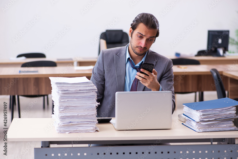 Young male employee unhappy with excessive work in the office Young male employee unhappy with excessive work in the office