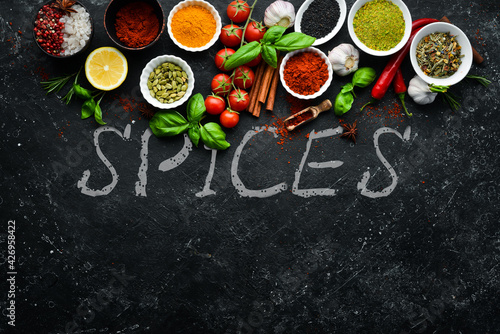 Set of colored spices in bowls and herbs on a black stone background. View from above. Top view.