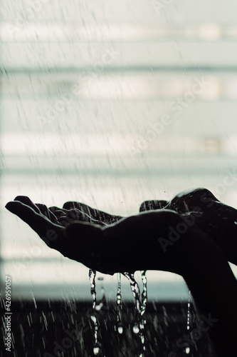 Silhouette of a man's hand under a shower against a backlit window.