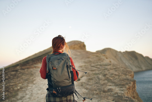 woman tourist climbs to the top of the bar along the road with a backpack on her back