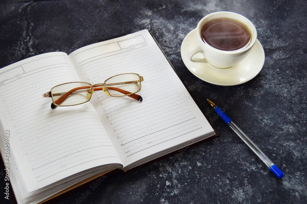 Remote online work, business concept diary with glasses and pen, hot cup of tea Remote online work, business concept diary with glasses and pen, hot cup of tea