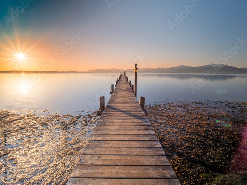 Chiemsee footbridge view during sunrise phase with alp mountain chain at the background