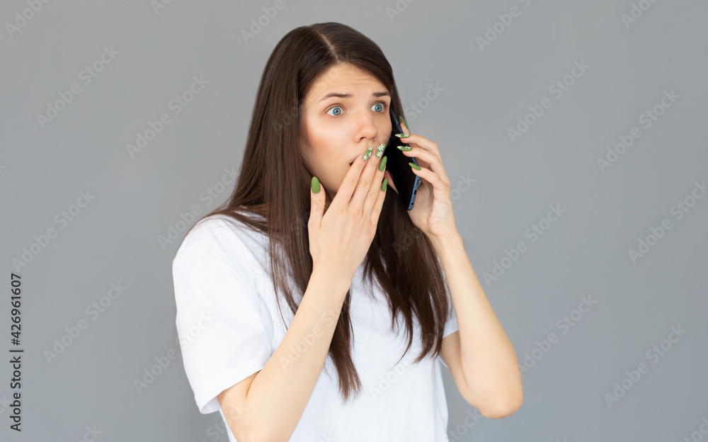 Headshot of shocked woman having argument talking via smartphone. Angry young female speak irritated by cell phone, hear bad news using phone. Portrait of girl with mobile isolated on gray Headshot of shocked woman having argument talking via smartphone. Angry young female speak irritated by cell phone, hear bad news using phone. Portrait of girl with mobile isolated on gray