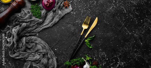 Kitchen banner: Spices, vegetables and cutlery on a black stone background. Top view. Free space for text.