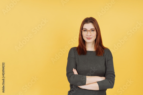Confident pert young woman wearing glasses standing with folded arms