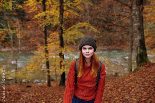 woman tourist in a sweater hat with a backpack near tall trees in autumn in the forest