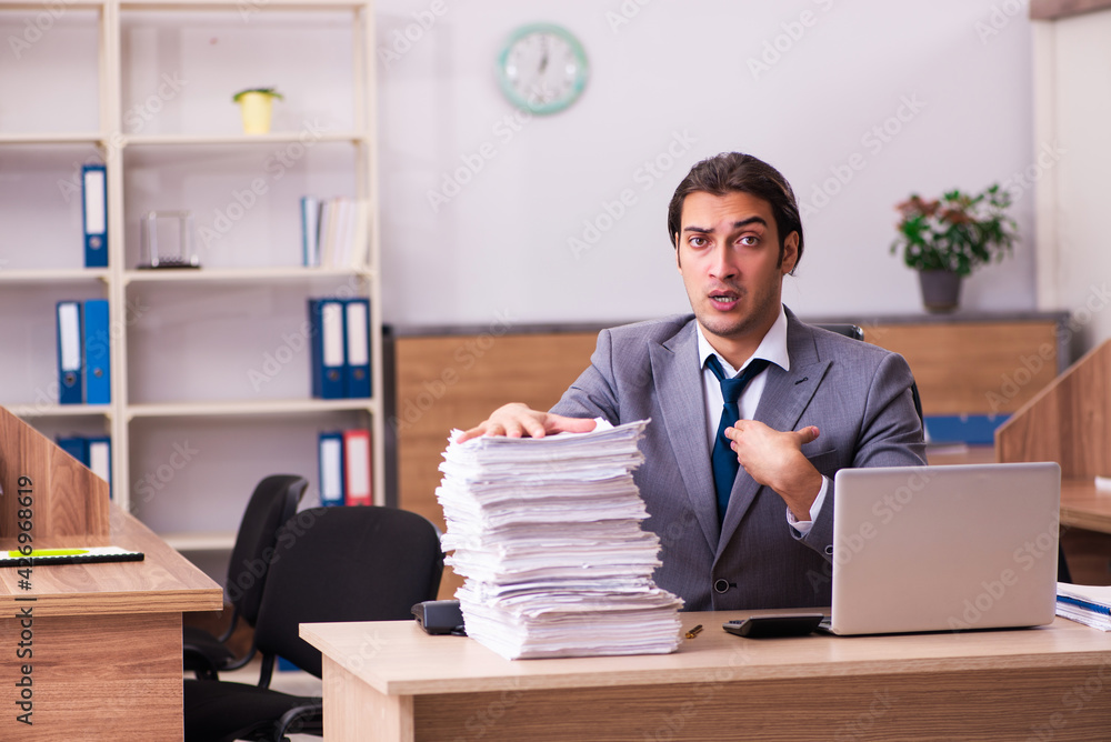 Young male employee unhappy with excessive work in the office Young male employee unhappy with excessive work in the office
