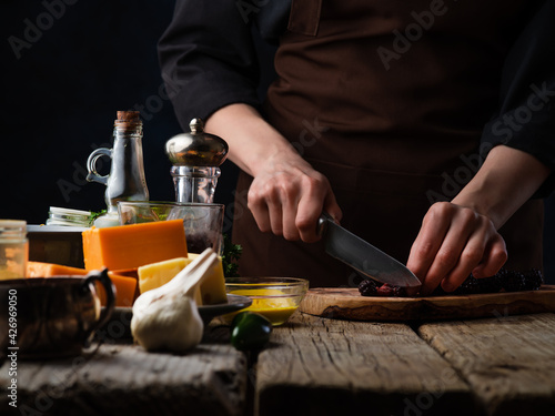 Chef cuts blackberries for cooking meat or salad on the background of ingredients.Various cheeses, garlic, tomatoes and spices.Culinary recipes