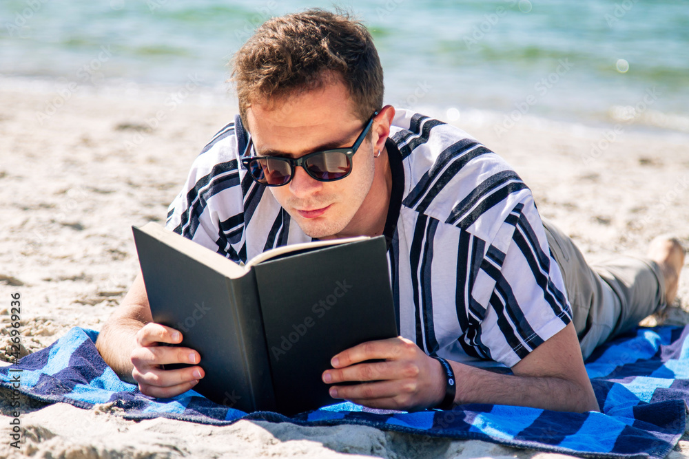 man lying relaxed on his towel on the beach reading a book