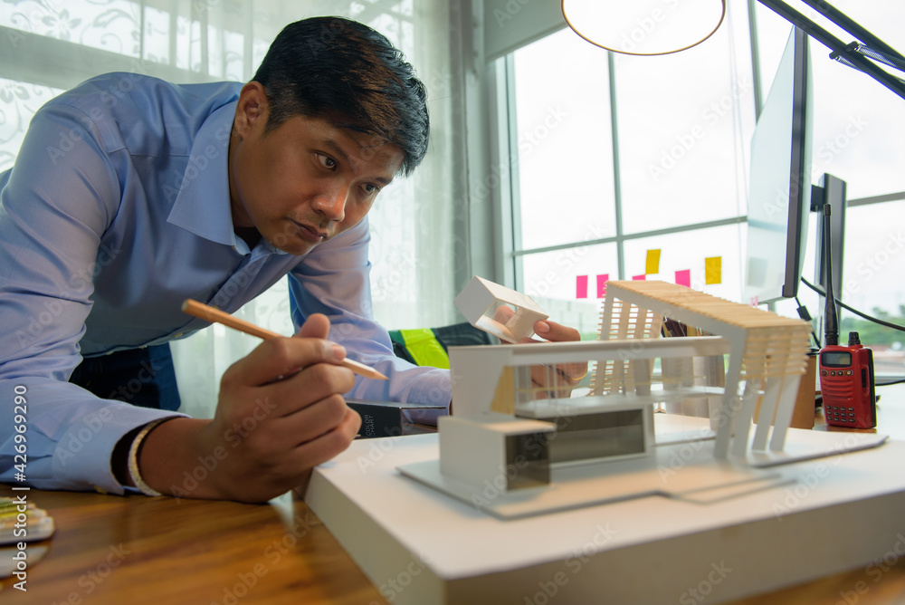 Architect-designer working with model of modern box house while thinking about concept of building and construction project before startup in the future. Architect-designer working with model of modern box house while thinking about concept of building and construction project before startup in the future.