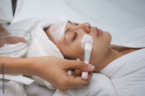 Asian young women lying relax using mask brush, moisturize their skin, making skin hydrated, helps with homemade apply face mask. Leisure activity at home.