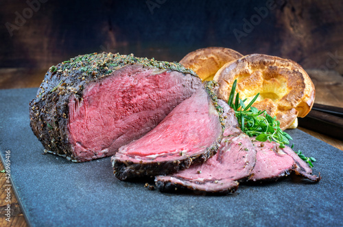 Traditional barbecue dry aged angus roast beef steak with Yorkshire pudding and herbs served as close-up on a black board