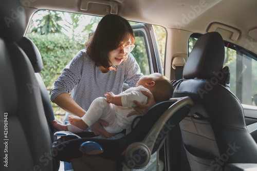 Asian young mother putting her baby son into car seat
