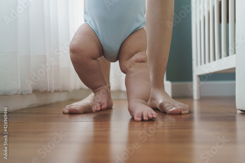 Foto Asian Mother holding her little baby hands learning to walk on wooden floor at home