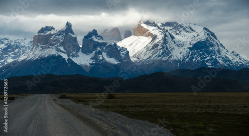road heading to huge rocky mountain range covered with snow under stormy clouds and sunbeams in awesome Patagonia  © Vitaliy Honor 