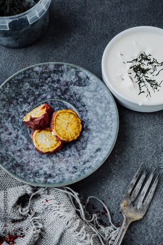 baked sweet potato slices in porcelain mug in dark kitchen with white cream sauce on rough burlap gray napkin. quick homemade yam recipes. country food. selective focus