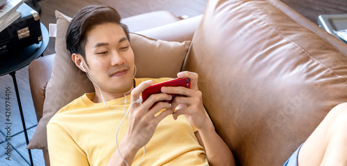 young asian male hand playing smartphone gaming online casual and leisure exiting and jpyful laydown on sofa on weekend at home quarantine activity ideas concept photo