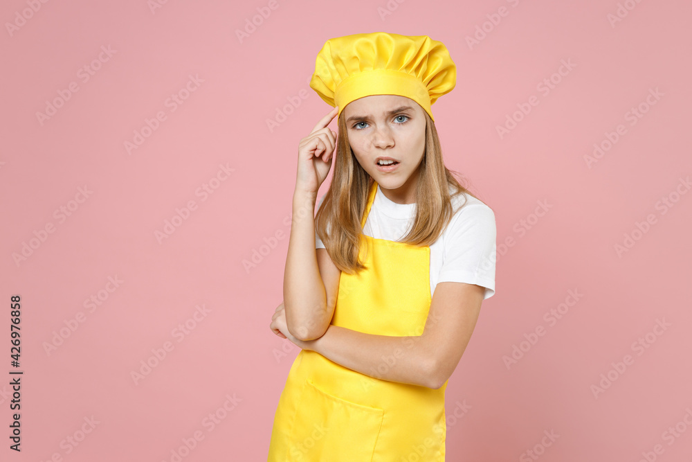 Teen thoughtful puzzled girl chef cook confectioner baker housewife wearing yellow apron white t-shirt toque cap prop up forehead isolated on pastel pink background studio portrait Food cake concept. Teen thoughtful puzzled girl chef cook confectioner baker housewife wearing yellow apron white t-shirt toque cap prop up forehead isolated on pastel pink background studio portrait Food cake concept.