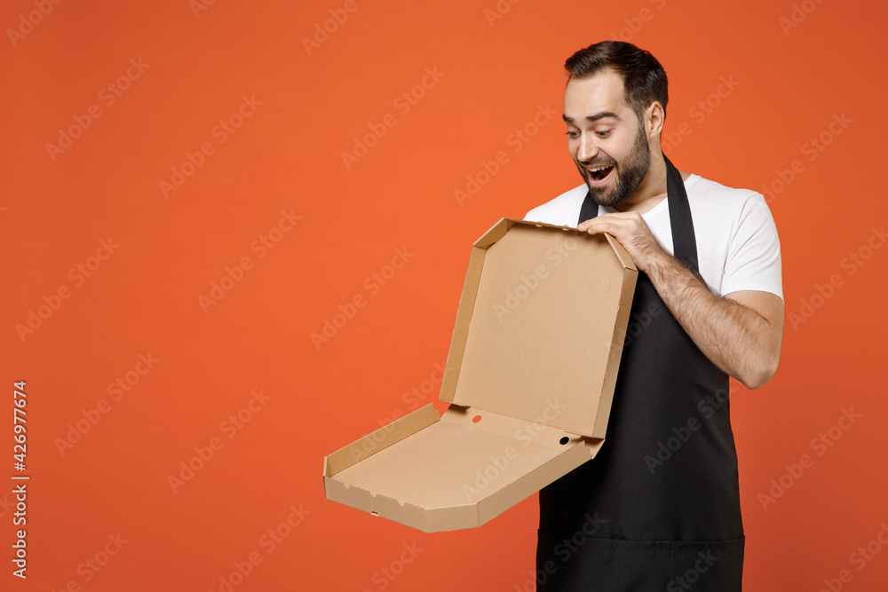 Young man 20s barista bartender barman employee in apron white t-shirt work coffee shop holding empty italian pizza in cardboard flatbox isolated on orange background Small business startup concept. Young man 20s barista bartender barman employee in apron white t-shirt work coffee shop holding empty italian pizza in cardboard flatbox isolated on orange background Small business startup concept.