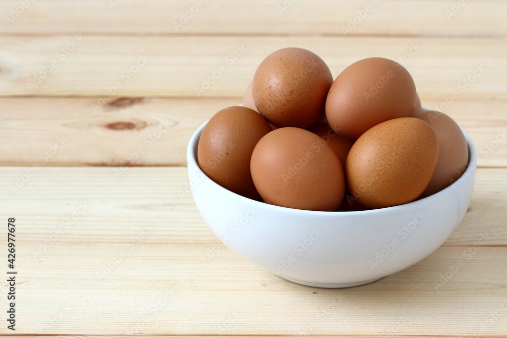 Organic eggs in a white bowl are placed on a wooden table. Organic eggs in a white bowl are placed on a wooden table.