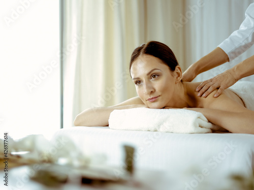 Pretty brunette woman enjoying procedure of back massage in spa salon. Beauty concept