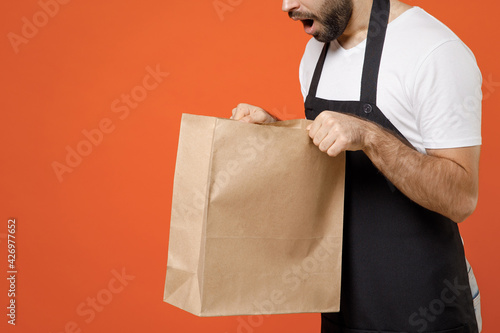 Closeup cropped shot shock male hands barista bartender barman employee in coffee shop hold delivery craft takeaway food brown bag mock up isolated on orange background Small business startup concept