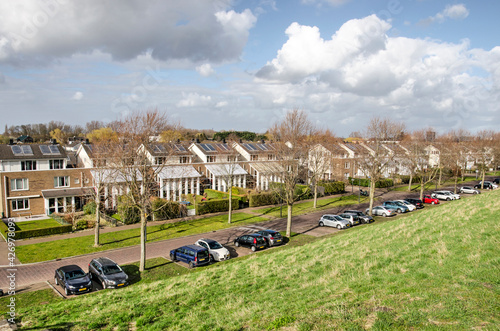 Rotterdam, The Netherlands, March 27, 2021: suburban row houses with solar panels and parked cars at the foot of a sound barrier in Nieuw Terbregge neighbourhood