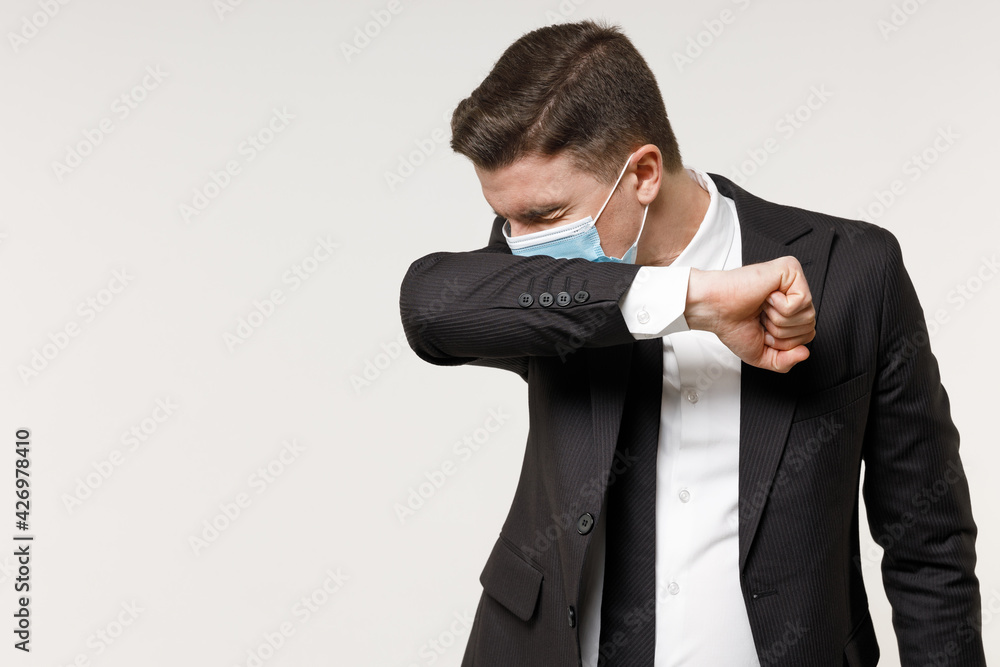 Young employee business corporate lawyer man in classic black suit tie sterile face mask from coronavirus covid-19 pandemic quarantine work in office sneeze into sleeve isolated on white background Young employee business corporate lawyer man in classic black suit tie sterile face mask from coronavirus covid-19 pandemic quarantine work in office sneeze into sleeve isolated on white background