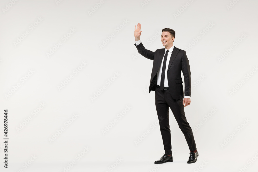 Full length young smiling successful employee business corporate lawyer man wear classic formal black grey suit shirt tie work in office walk waving hand greeting isolated on white background studio. Full length young smiling successful employee business corporate lawyer man wear classic formal black grey suit shirt tie work in office walk waving hand greeting isolated on white background studio.
