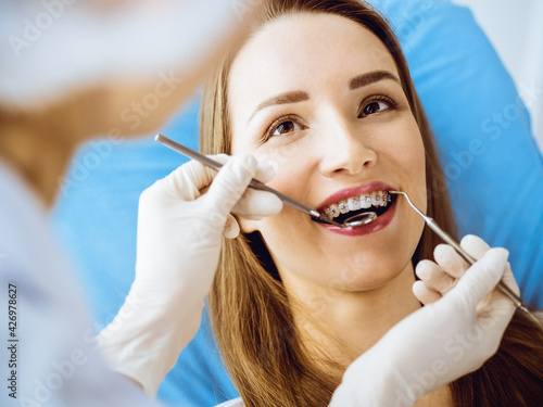 Smiling young woman with orthodontic brackets examined by dentist in dental clinic. Healthy teeth and medical care concept