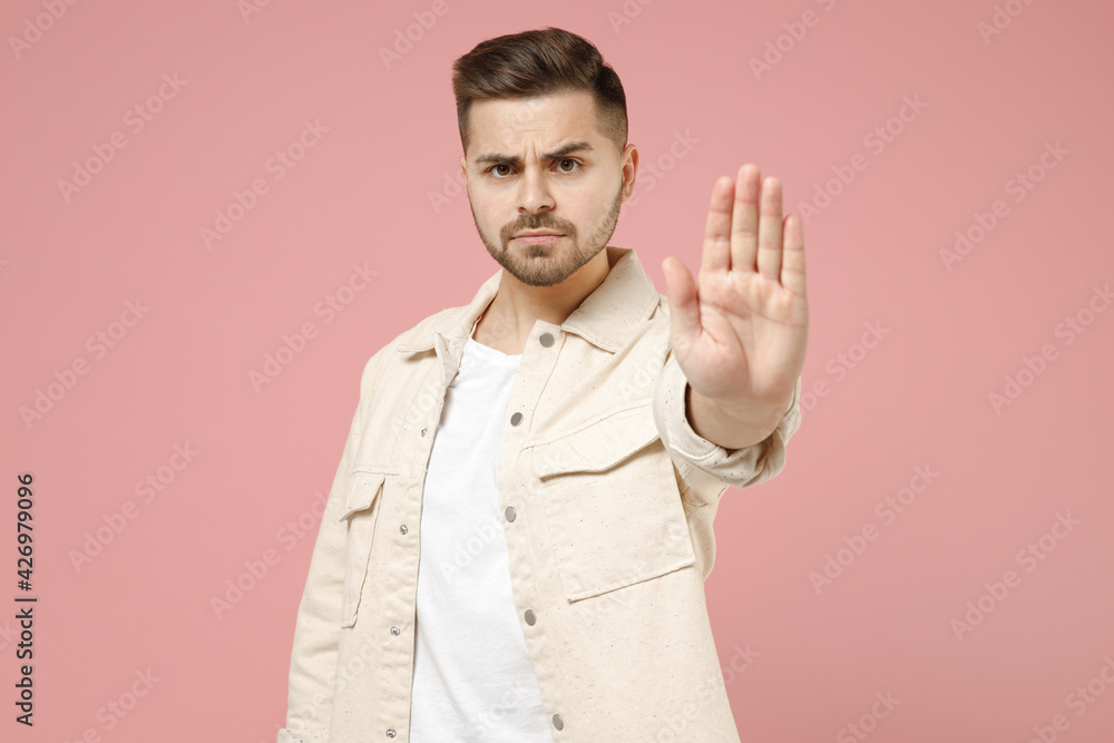 Young serious strict trendy caucasian man 20s wearing jacket white t-shirt do stop palm gesture refusing saying no isolated on pastel pink color background studio portrait. People lifestyle concept. Young serious strict trendy caucasian man 20s wearing jacket white t-shirt do stop palm gesture refusing saying no isolated on pastel pink color background studio portrait. People lifestyle concept.